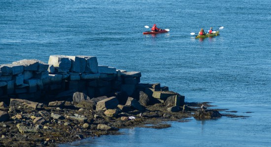 Two kayaks with people on ocean water close to rocky shore